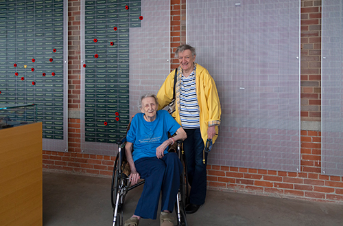 A woman in a wheelchair sits in front a wall covered in green plaques.