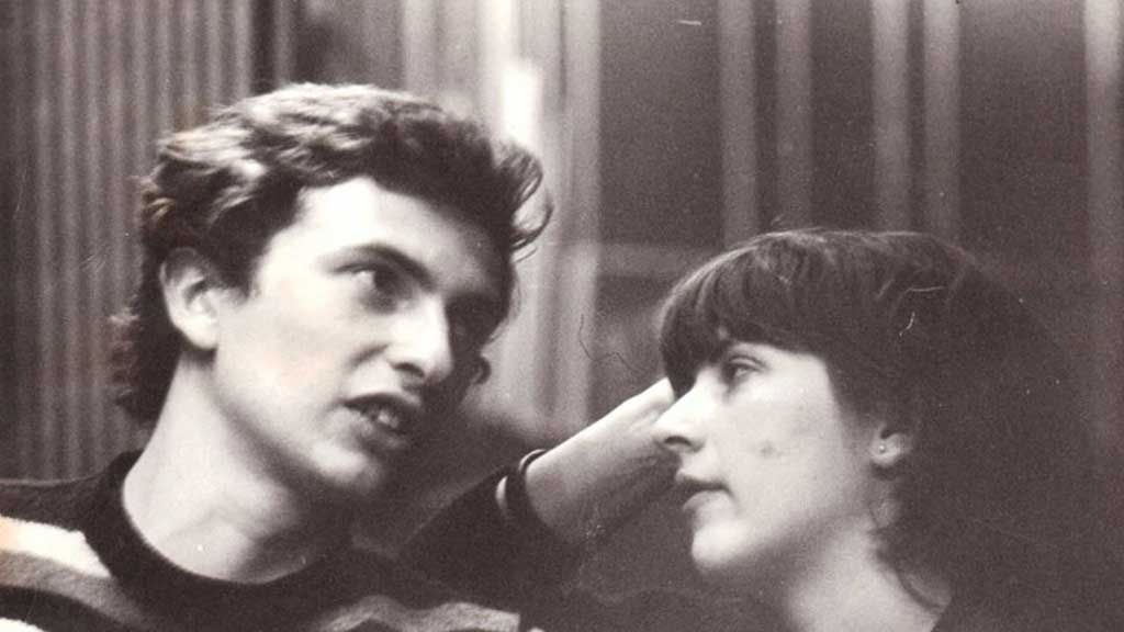 A black and white photo of a man and woman deep in conversation. Leaning her head on her hand, she watches him speak. Their heads are mere inches apart.