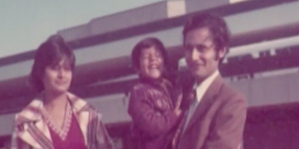 A seventies-era photograph of a family of three, posing for the camera outside an airport.