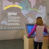 A young girl is looking at a screen which shows changing immigration trends on a map.
