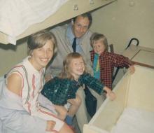A family of four are all sitting on a small, bottom, ship bunk.
