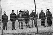 Archival image of several men standing behind a barbed-wire fence.