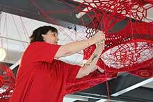 An artist works with red string to create a hanging craft.