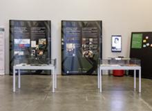 Roma People in Canada exhibit with informational panels, two glass display cases, and a black board with posters and notes.