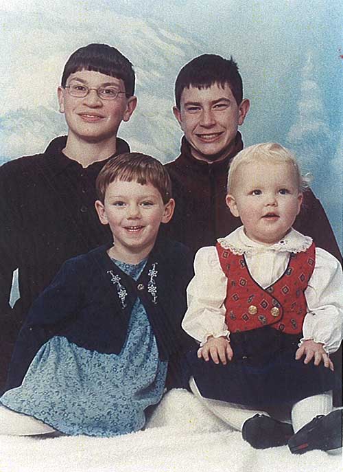 Two young men standing behind two cute children for a photo.