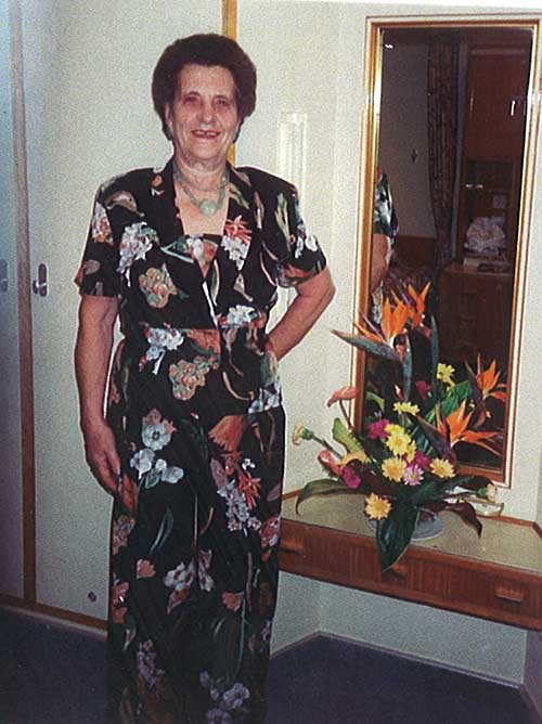 Beautiful woman wearing black flowery dress is standing in front of a dressing table.