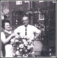 Man and woman outside home with flowers.