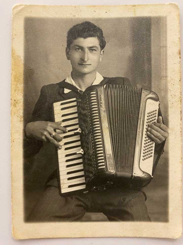 A young man smiles for the camera as he plays his accordion.