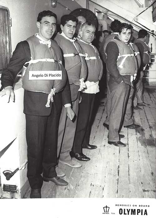 Four men wearing life vests and standing on ship’s deck.