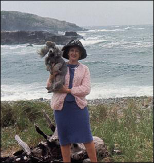 A young woman with a dog stand on the sea shore.