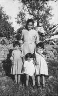 Woman with three children in front of tree and brick wall.