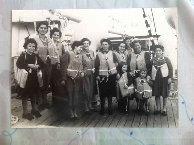 A group of people wearing life jackets stand on the deck of a ship.