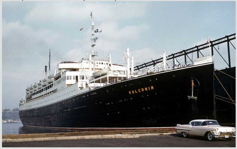 A ship is shown docking at a pier, with old-fashioned car in a parking lot.
