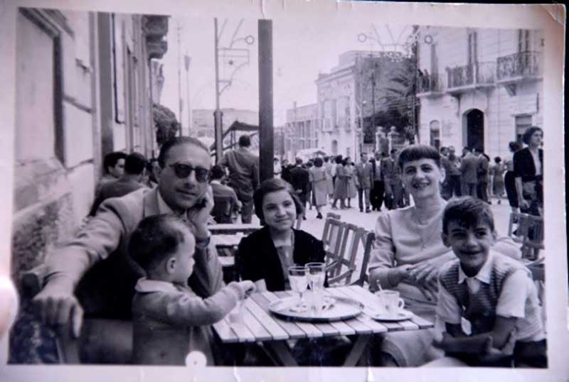 A young family sit at an outdoor cafe with pizza on the table.