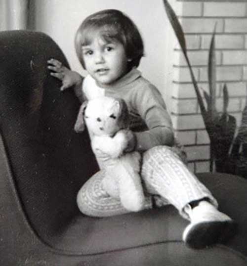 A young girl sits on a chair and is holding a teddy bear.