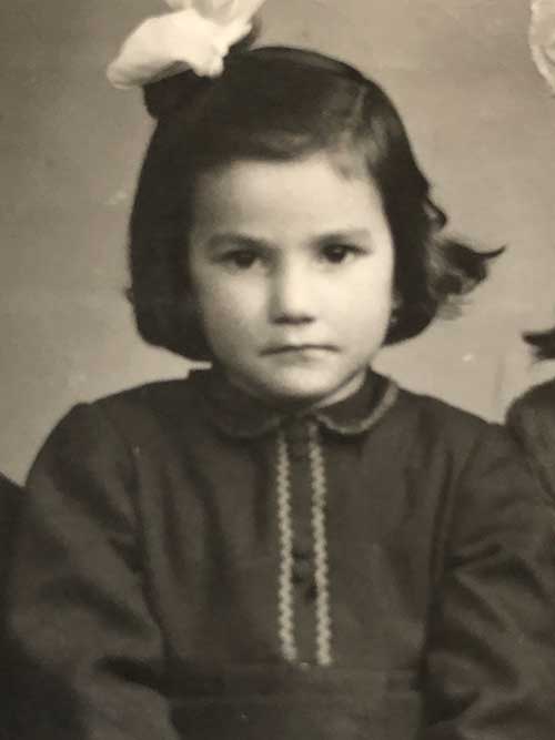 A young girl stares unsmiling at the camera, there is a big bow on her head.