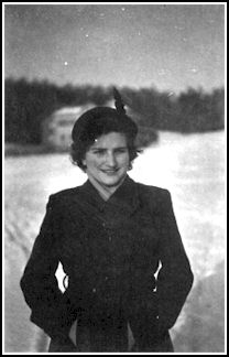 Young woman wearing winter coat and hat, standing in the snow.