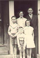 Young man and woman with three children, standing on porch steps.