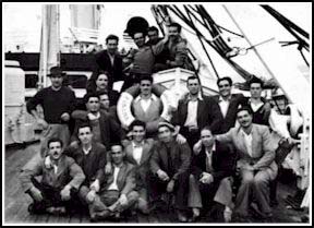 Large group of young men seated in and around a life boat on board ship.