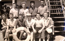 Several young men seated and standing behind a ship's life preserver.