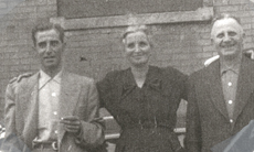 Woman in between two men, standing in front of building.