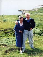 Catherine and Gordon as older couple, standing on grassy hill. 