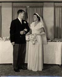 Photo of bride and groom on wedding day, in front of banquet table.