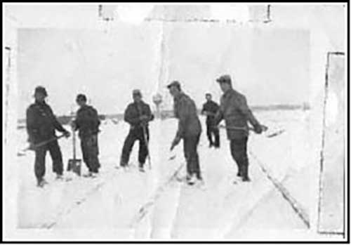 Old photo showing 7 men shovelling snow off newly-built train tracks.