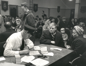 Man and woman seated at a desk with an immigration officer in a busy room.