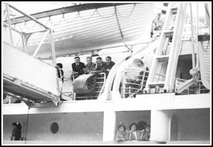 Young men viewed leaning on railing on deck of ship.
