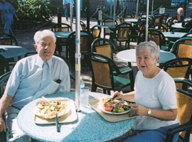 Older couple seated at restaurant patio table, with plates of food in front of them