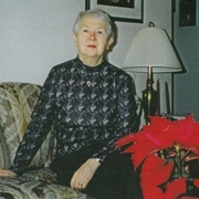 Older woman seated on couch with poinsettia in foreground.