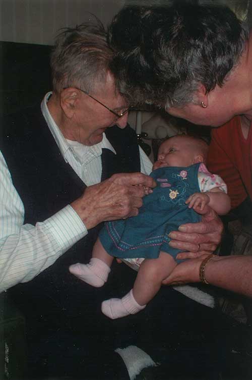 An elderly man looks fondly at a cute little baby in his lap.