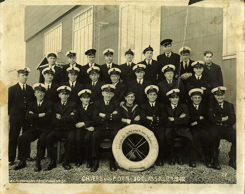 Sailors and officers in uniforms sit and pose for the camera.