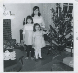Three young girls standing next to Christmas tree.