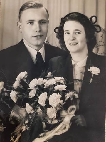 A sepia-toned portrait of a white Dutch couple smiling with flowers smiling in formal clothing.