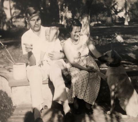 A sepia-toned photo of a white Dutch man and woman sitting outside with a baby and a large dog.