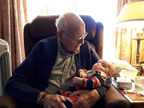 An elderly white man sitting in a chair and holding a baby.