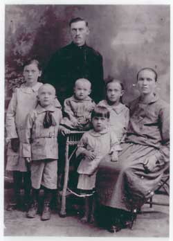 Old family portrait of mother sitting and five children and father standing on her right.