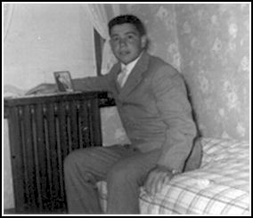 Young man seated on bed by window of room.