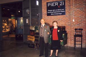 Man and woman standing under Pier 21 sign, in front of luggage display.
