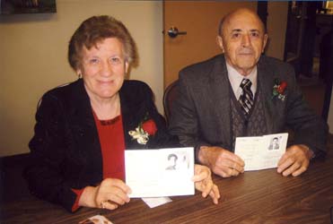 Man and woman seated at table, wearing rose corsages and holding passports open.