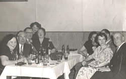 Men and women on both sides of a table filled with bottles and glasses.