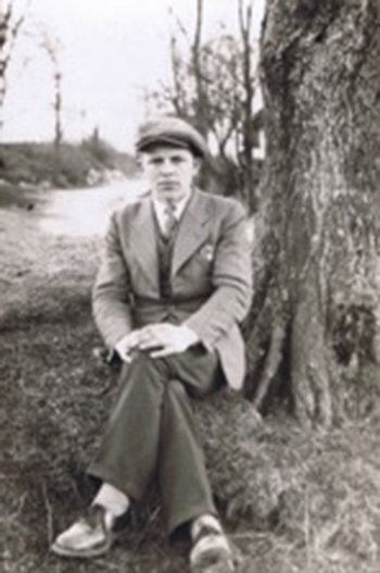 A young man is sitting on a tree stump with his legs crossed.