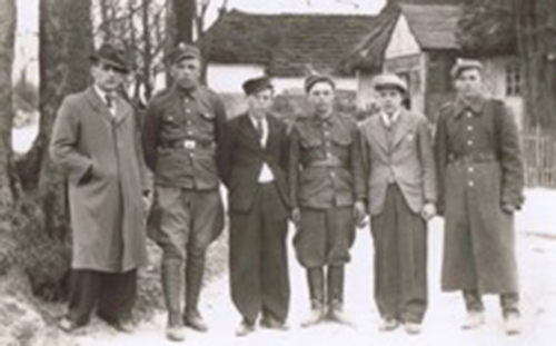 Six well-dressed men are standing in front of houses and trees.