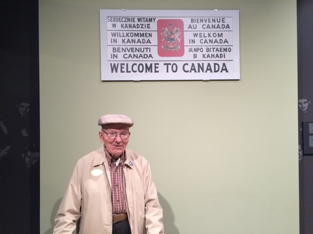 A young man is standing next to a sign saying Welcome to Canada.