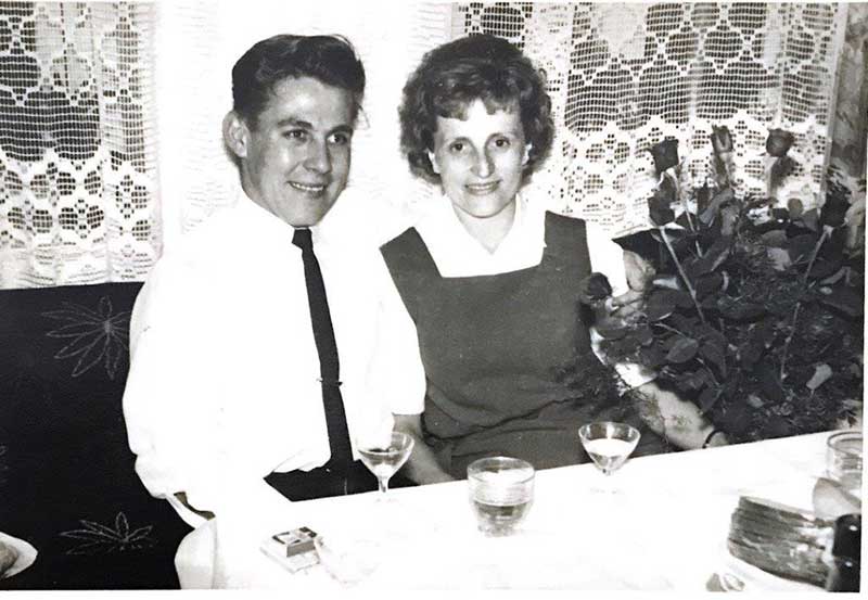 A young man and woman sit side by side as they drink wine.