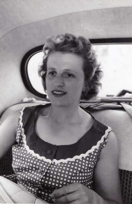 A young woman in a sleeveless dress sits in the back seat of a car.