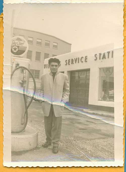 A young man stands in front of a service station next to a gas pump.