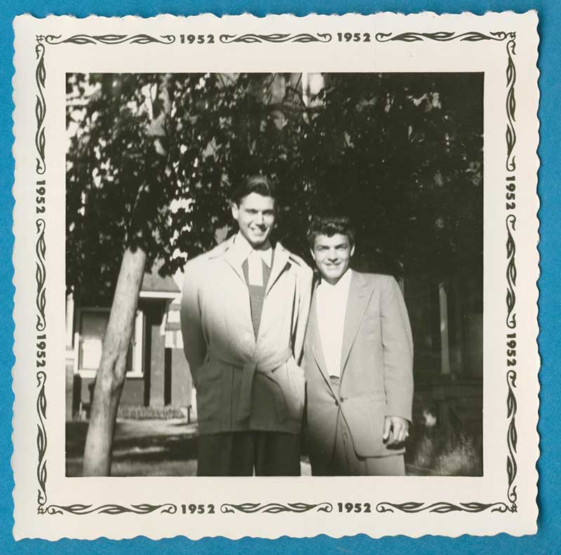 Two young men are standing next to some trees as they have their photo taken.